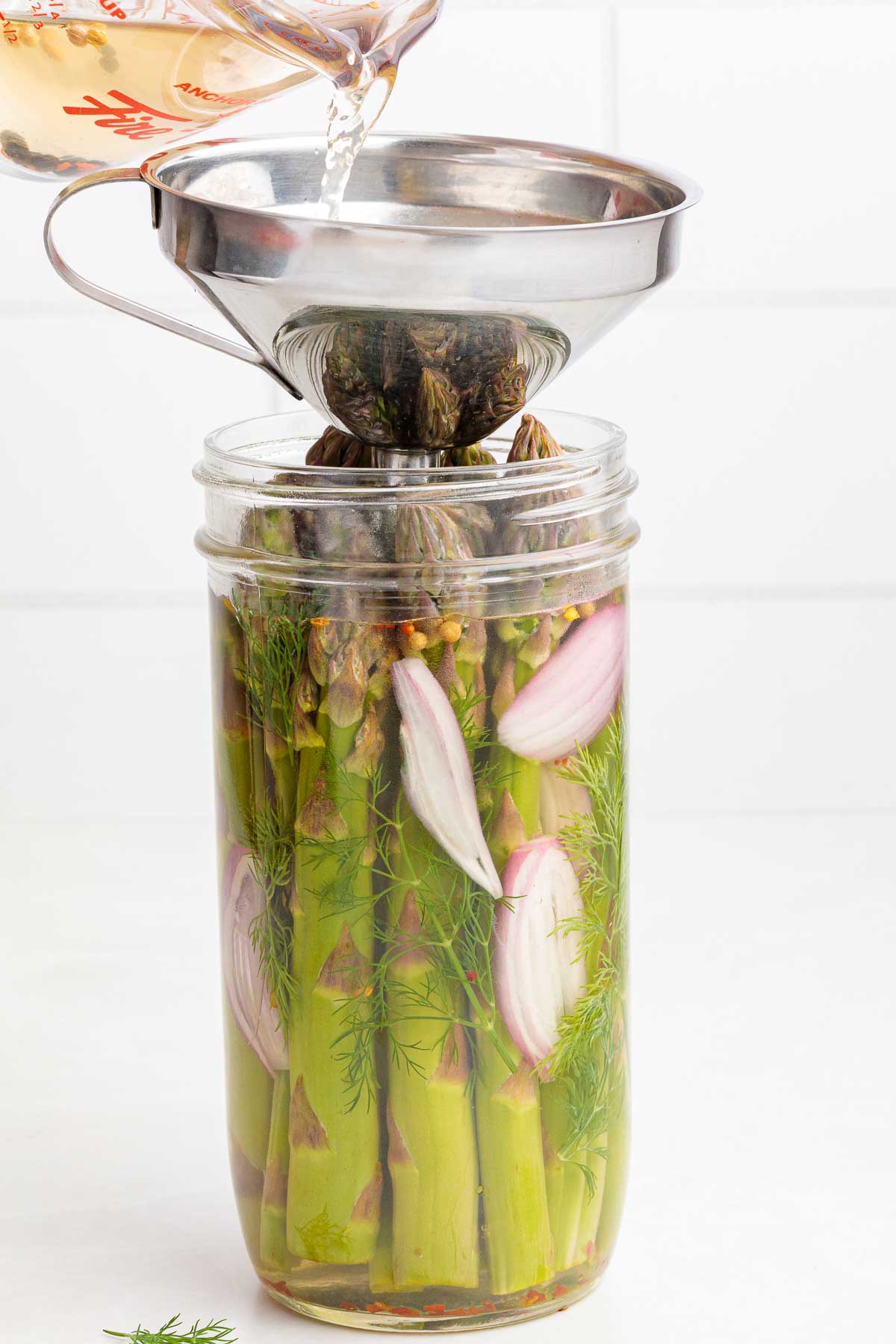 pouring the brine solution over a jar of asparagus for quick refrigerator pickles