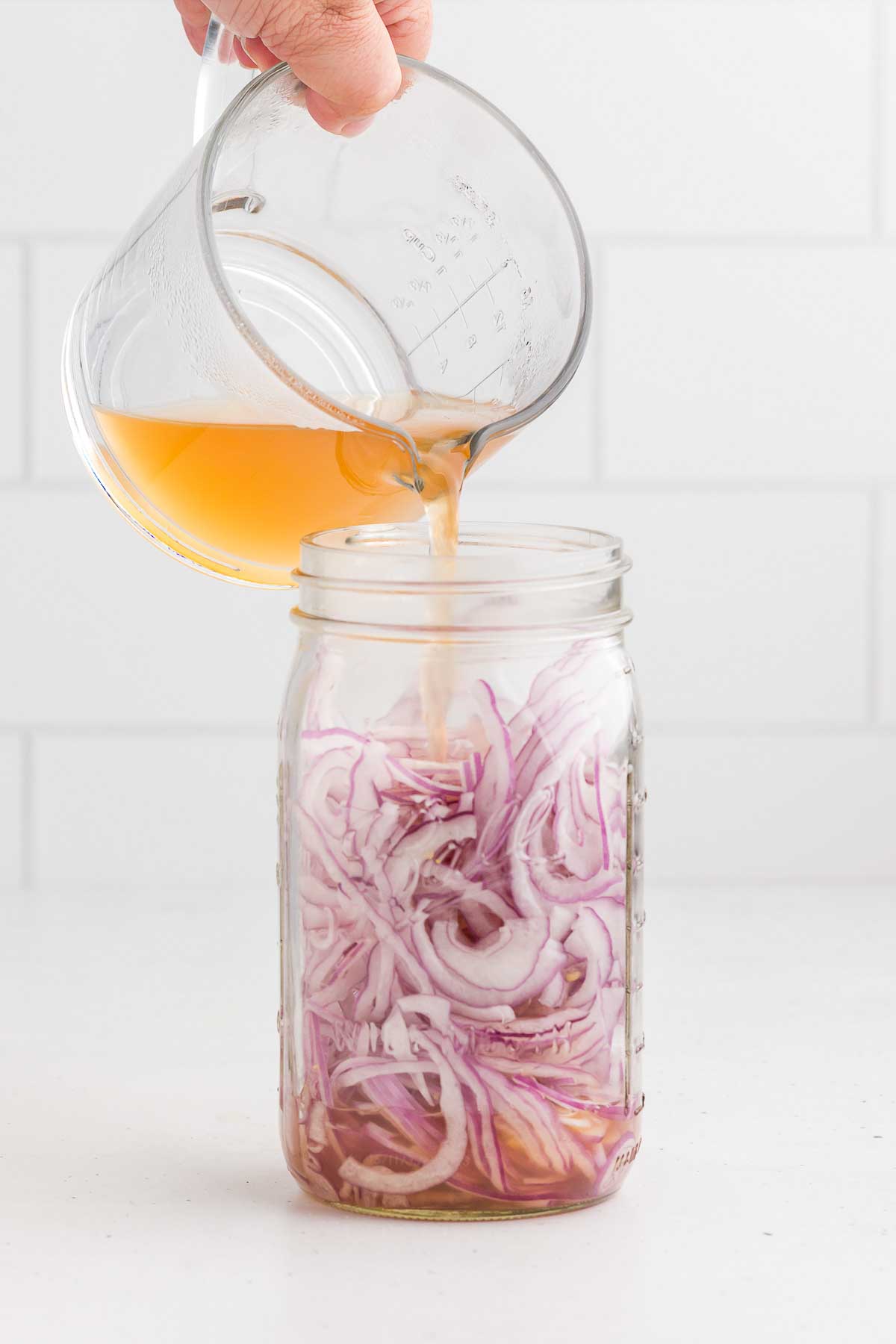 thinly sliced red onions in a mason jar with the brine being poured over the top for quick-pickled red onions