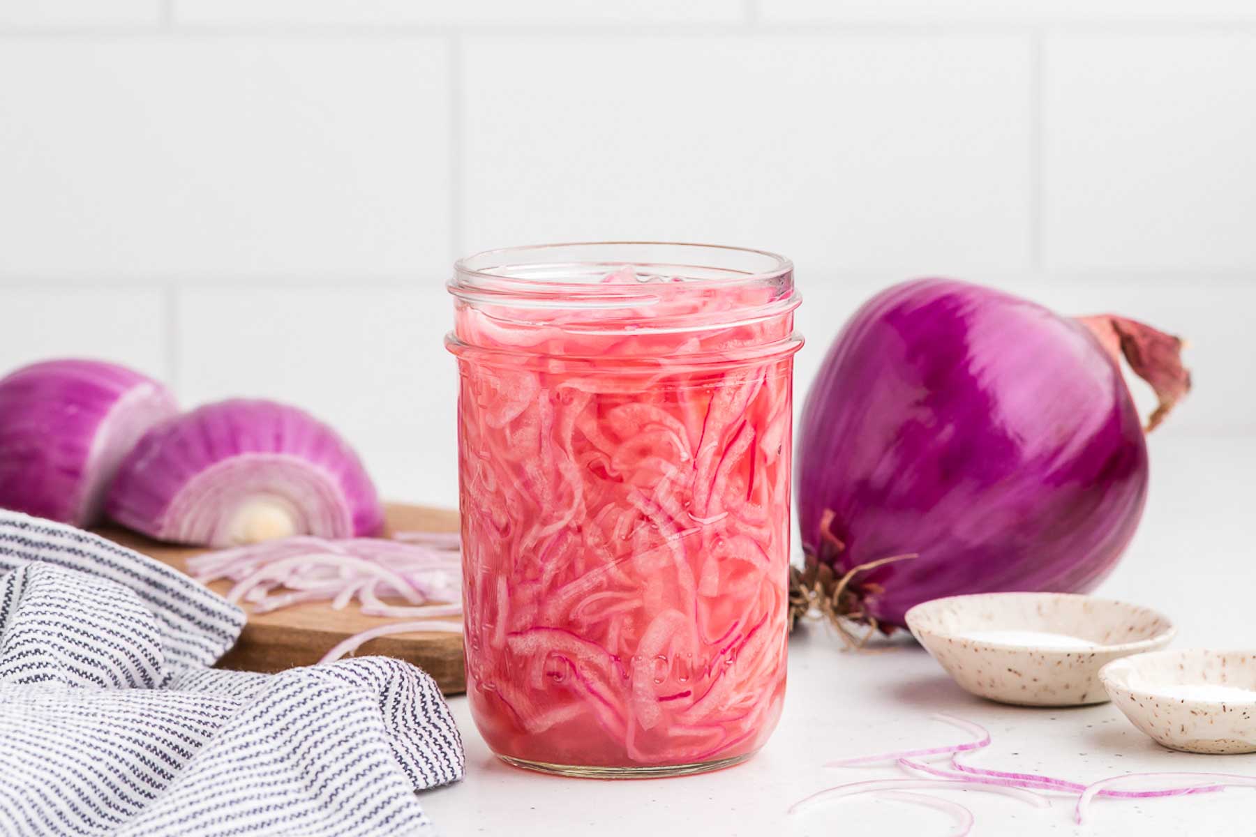 quick-pickled red onions in a mason jar with red onions in the background