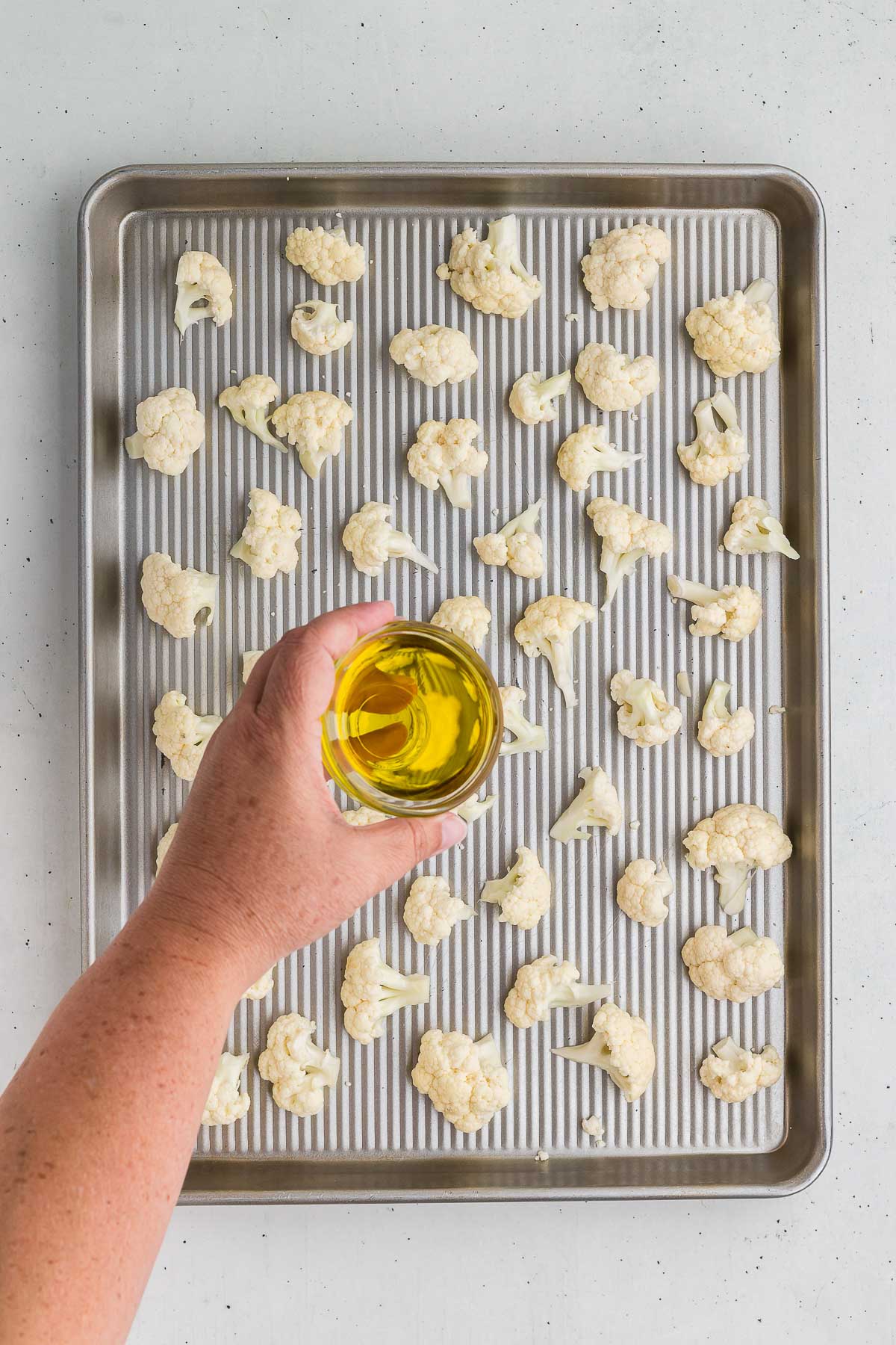Pouring olive oil over cauliflower for Roasted Cauliflower