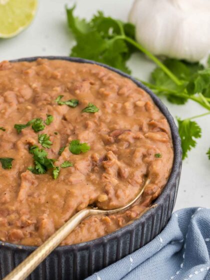 A gold spoon scoops up a serving of Homemade Refried Beans in a black bowl