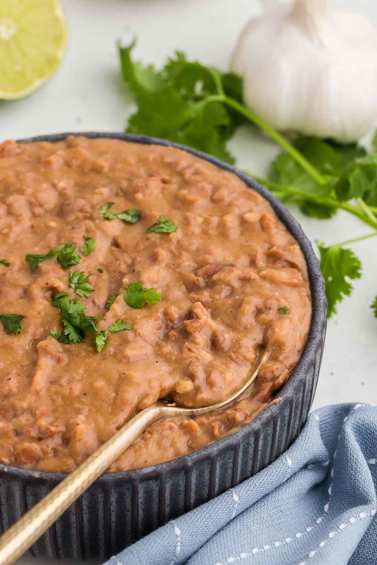 A gold spoon scoops up a serving of Homemade Refried Beans in a black bowl