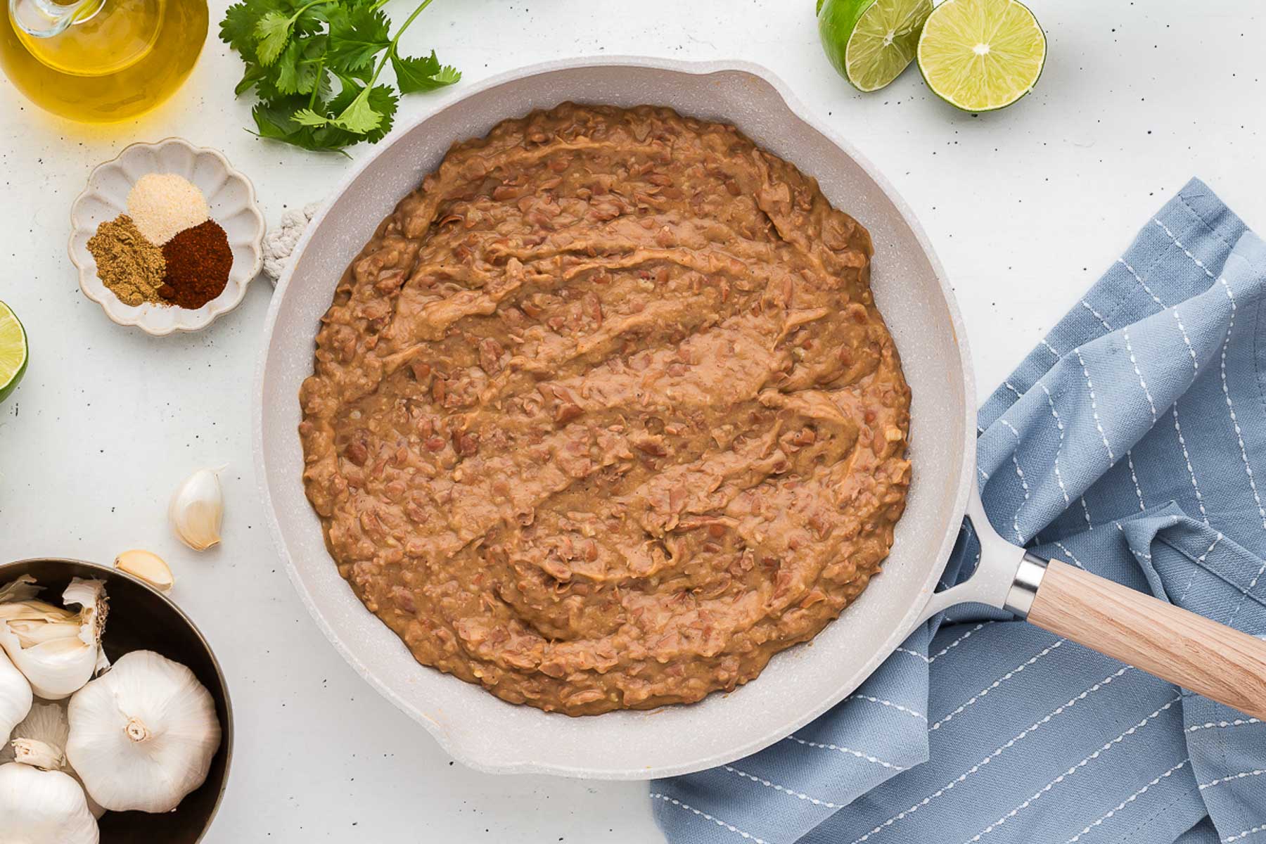 Homemade Refried Beans in a white skillet with ingredients in background