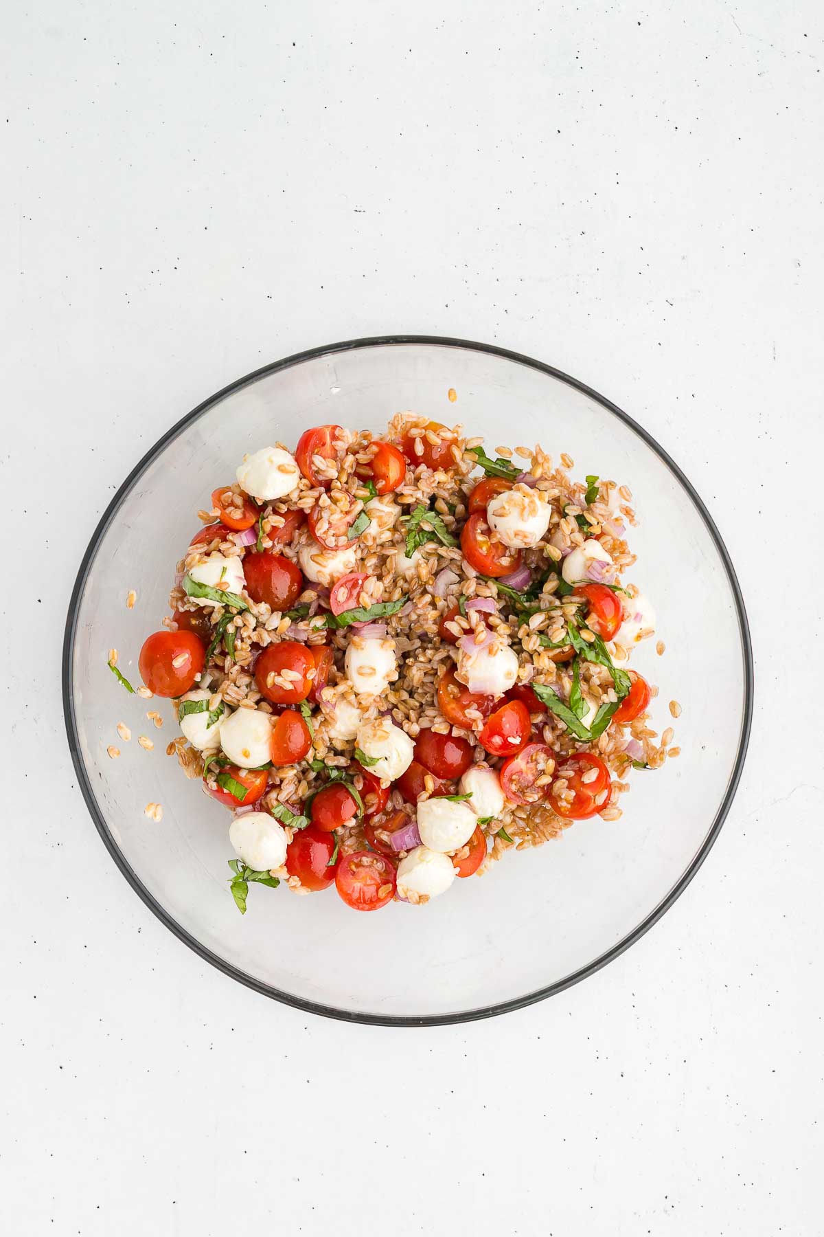 top view of farro caprese salad in a large glass bowl, freshly tossed