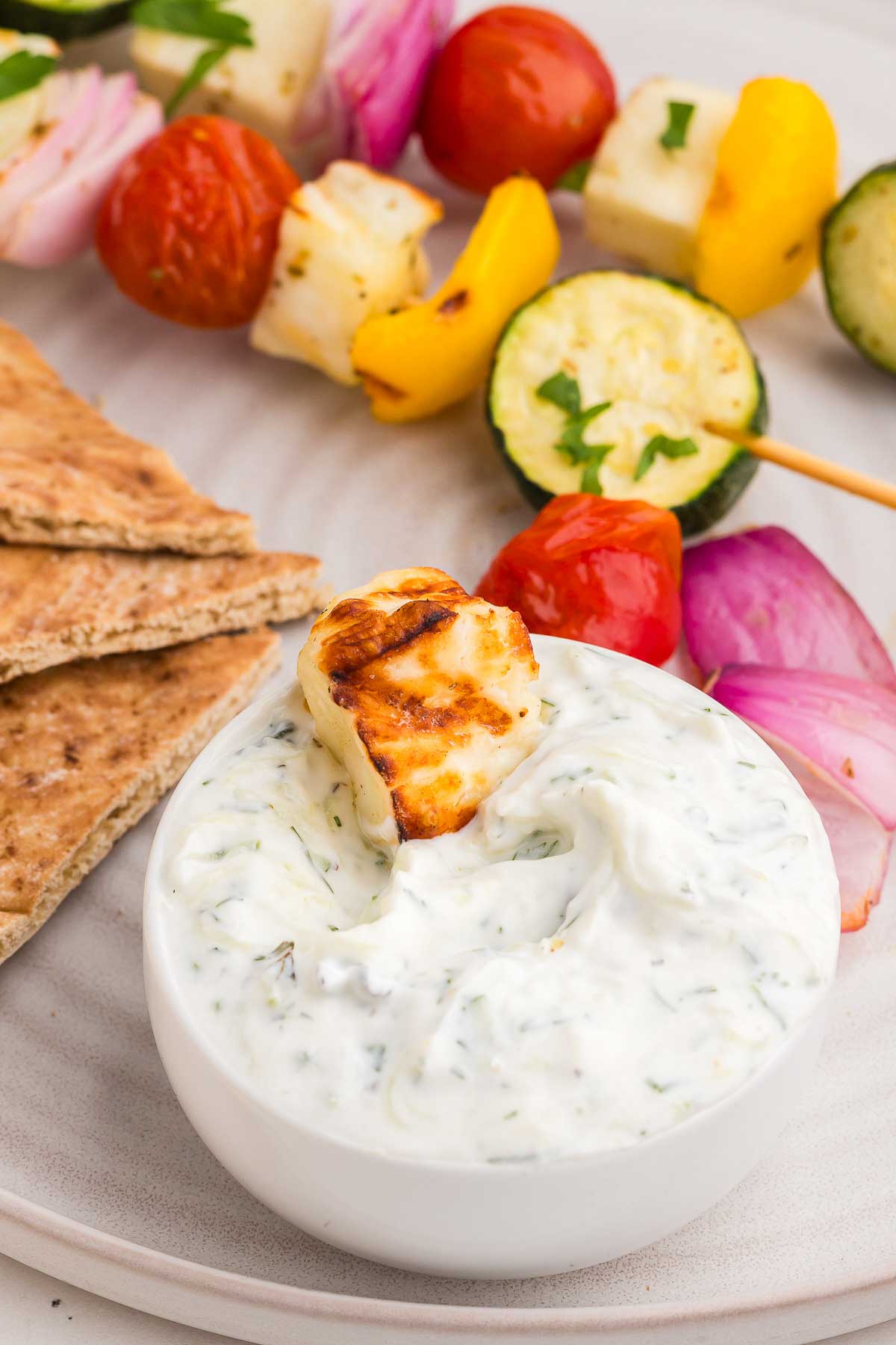 a piece of grilled halloumi dipped in a bowl of tzatziki
