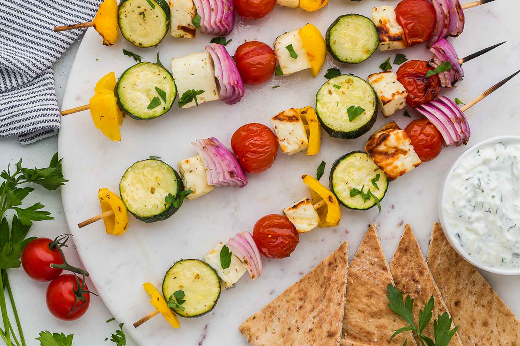 Grilled halloumi and vegetable skewers with pita bread on a white plate