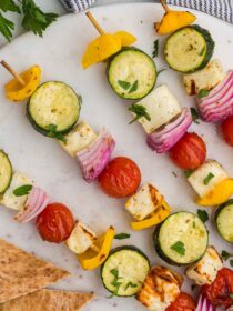 four grilled halloumi and veg skewers on a white plate