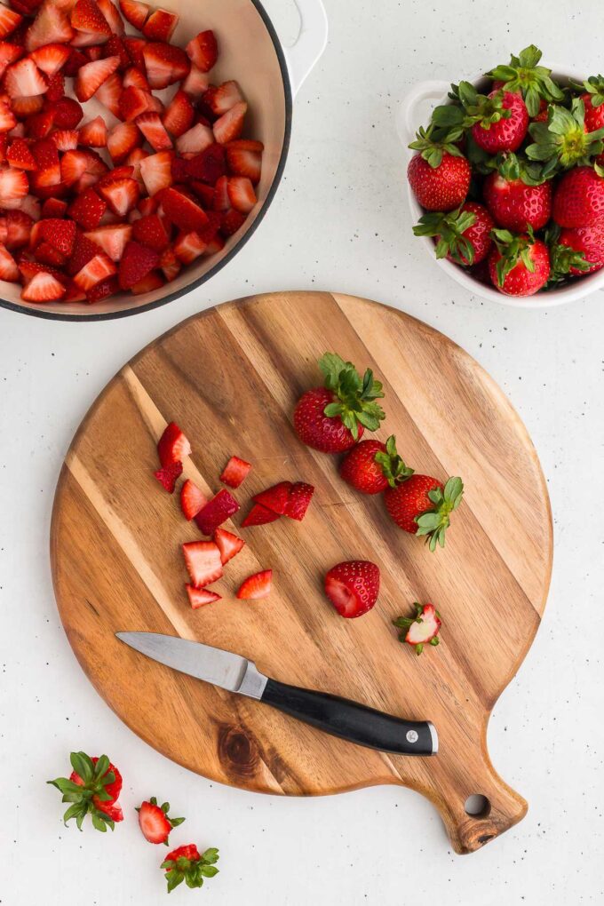 strawberries on a round cutting board being chopped for strawberry sauce.