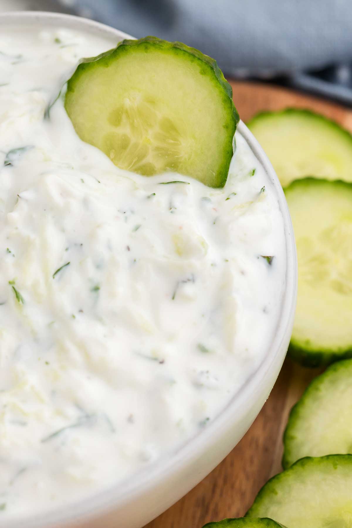 A close-up of a bowl of tzatziki sauce with a cucumber dipped in it