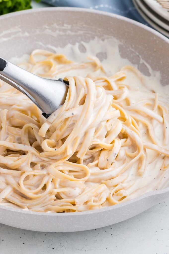 tongs swirl pasta in a cream cheese sauce