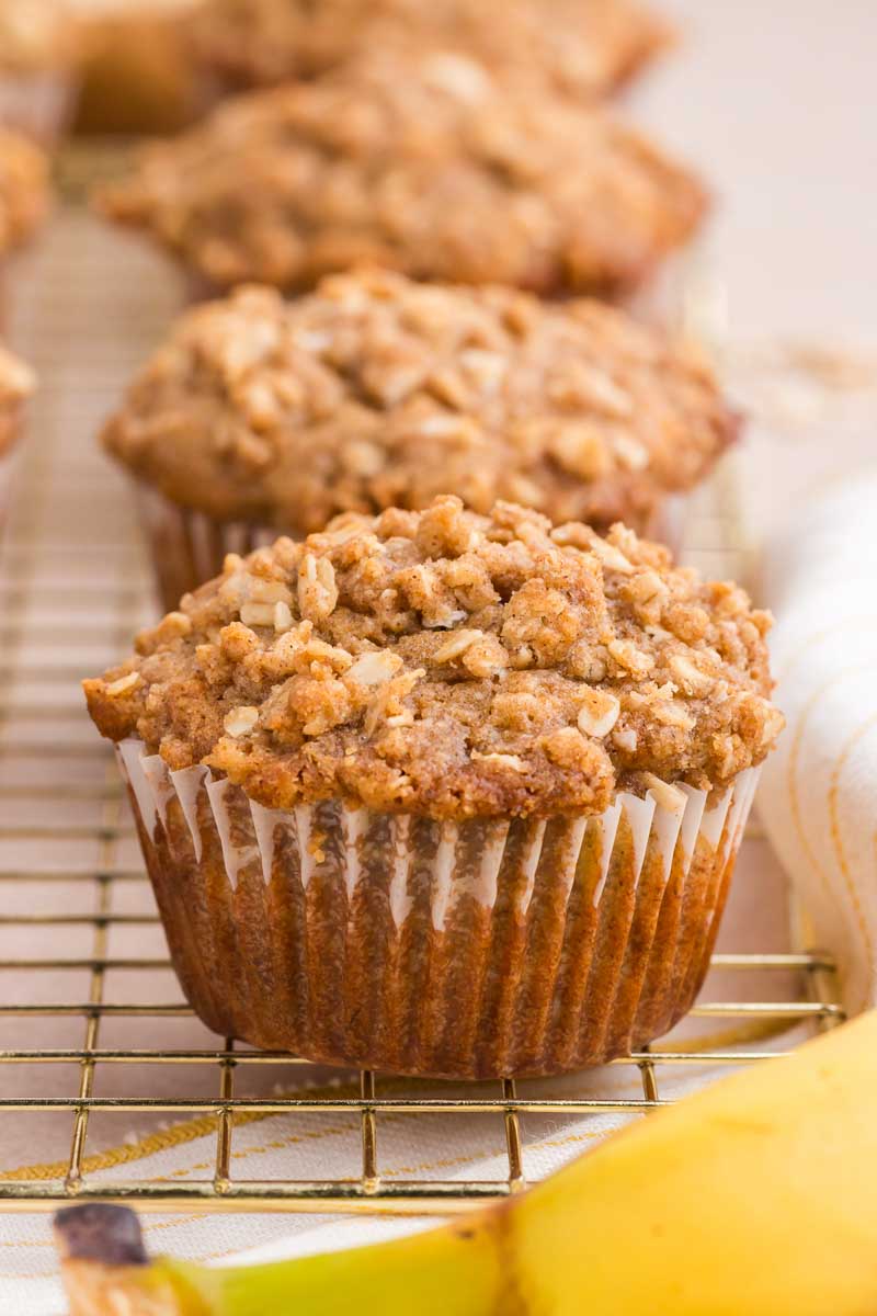 three banana streusel muffins lined up on a wire rack with a banana in the foreground
