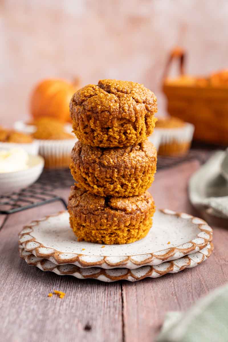 stack of three Blender Pumpkin Muffins on a plate with a distressed wood background