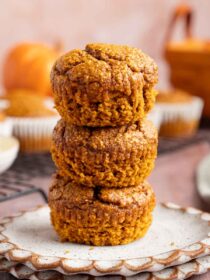 stack of three Blender Pumpkin Muffins on a plate with a distressed wood background