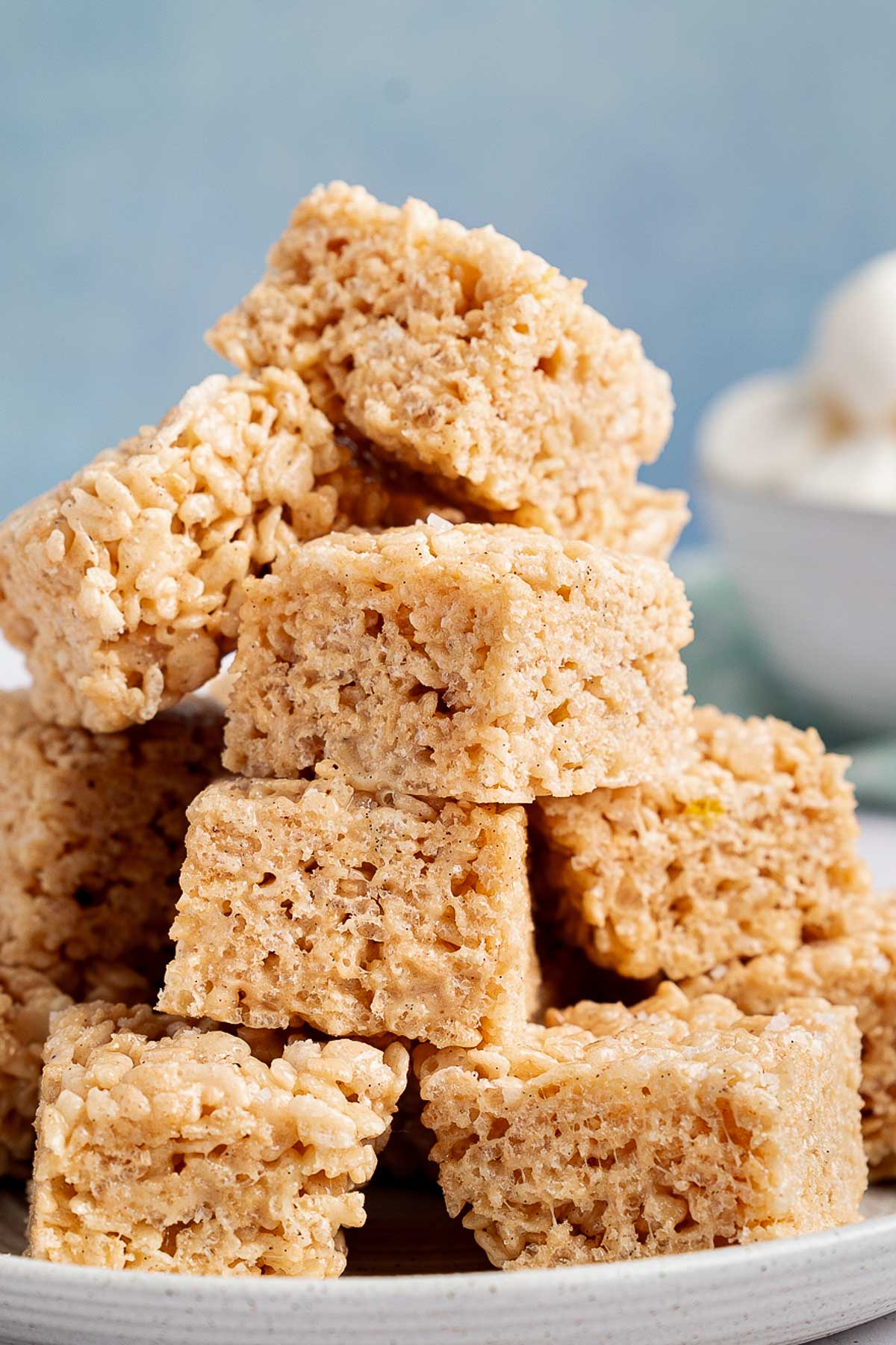 A tall stack of brown butter Rice Krispie treats on a white plate with a blue background