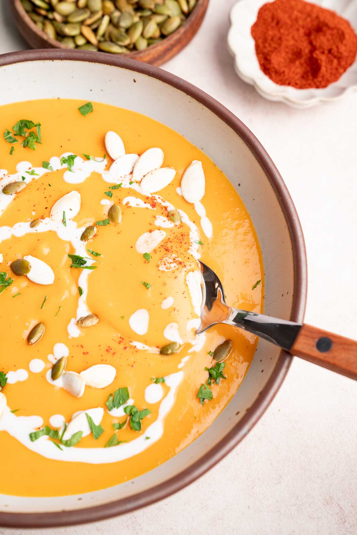 top view of a white bowl full of roasted butternut squash soup with a spoon and pepitas in the background