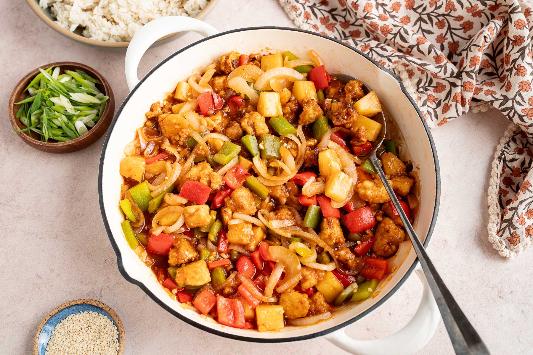 sweet and sour tofu in a skillet with scallions in a bowl next to it