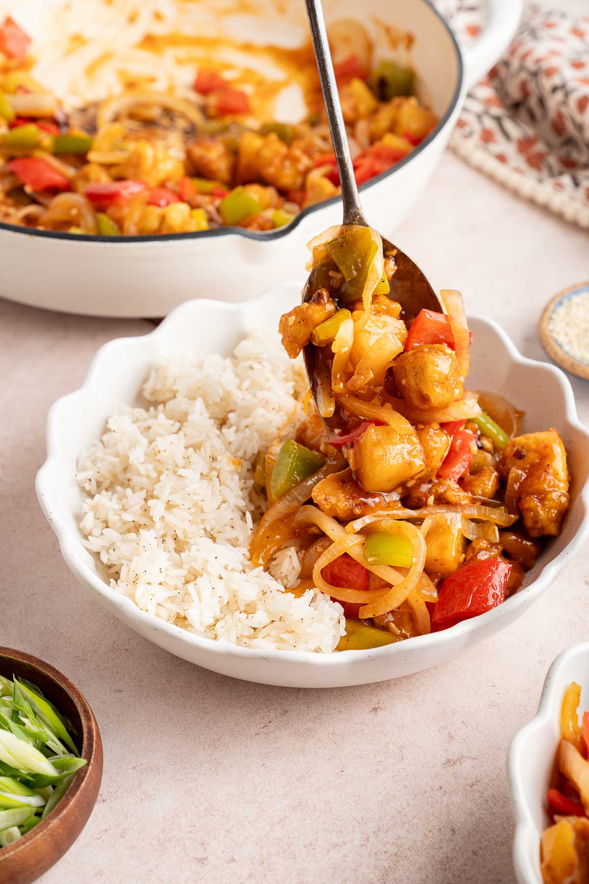 spooning sweet and sour tofu into a bowl with rice